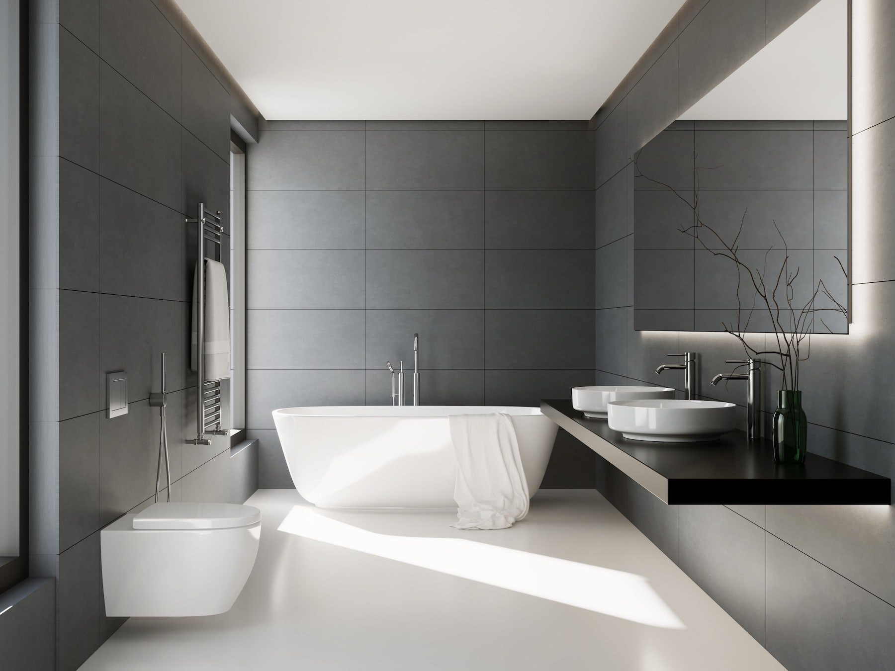 A bathroom tiled floor to ceiling in grey, with a freestanding bath and a wall-hung toilet.
