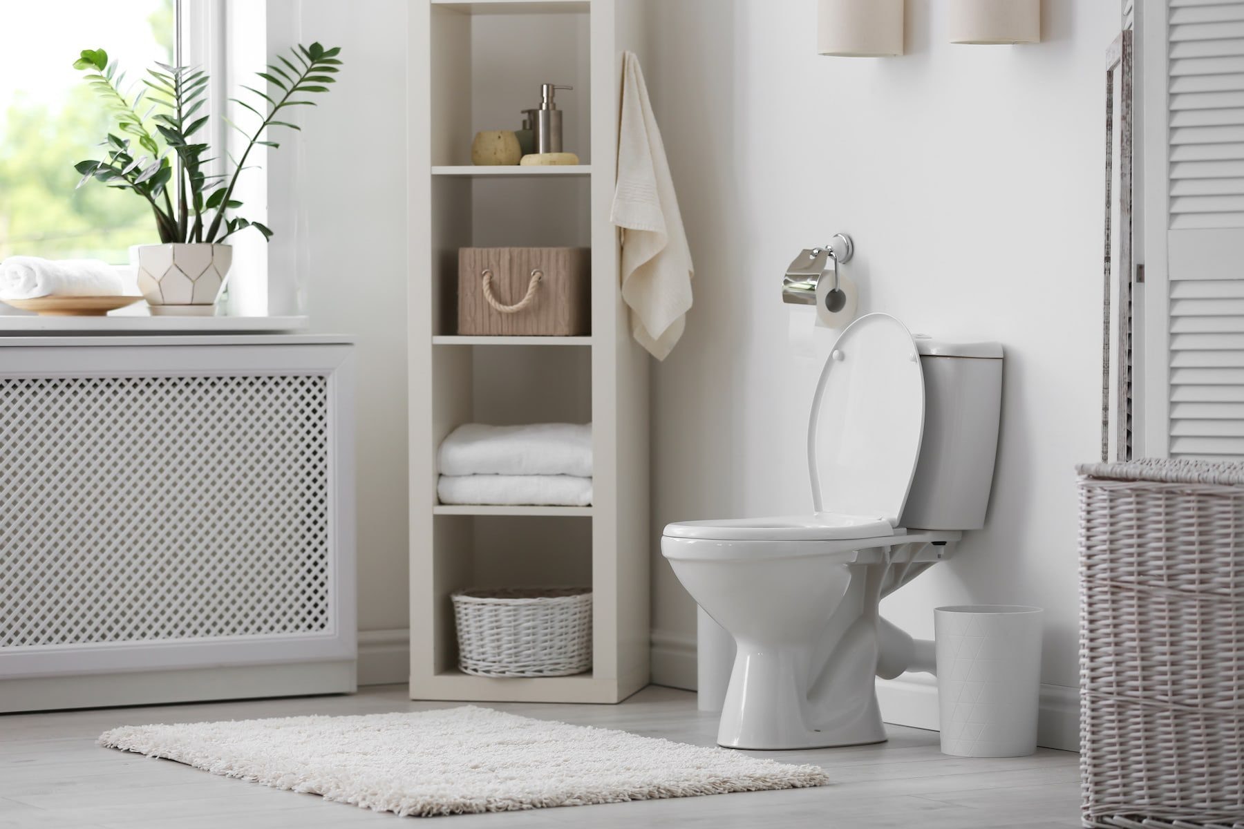 A simple white bathroom with a close-coupled toilet, a pedestal basin and open shelving with baskets.