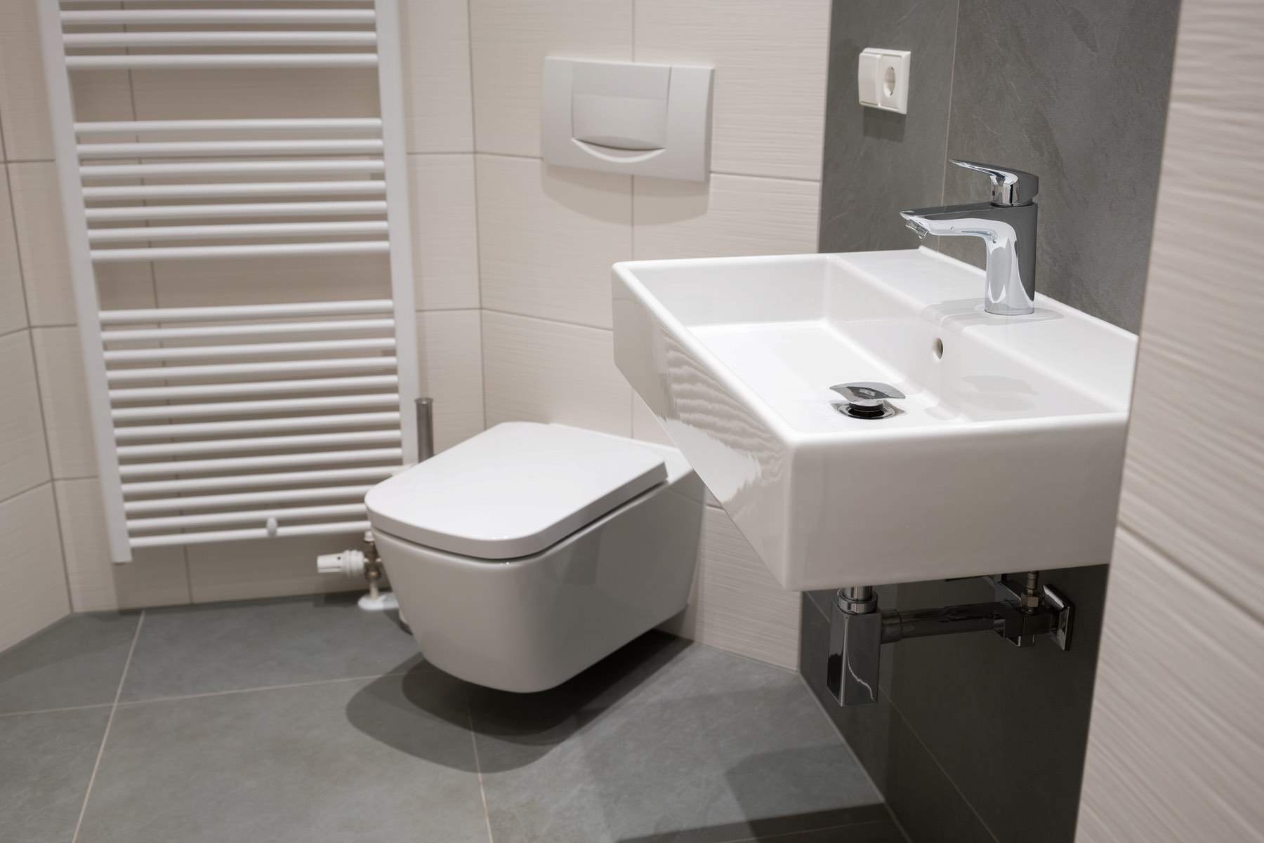 A small cloakroom with a wall-hung toilet, a compact basin and a white heated towel rail.