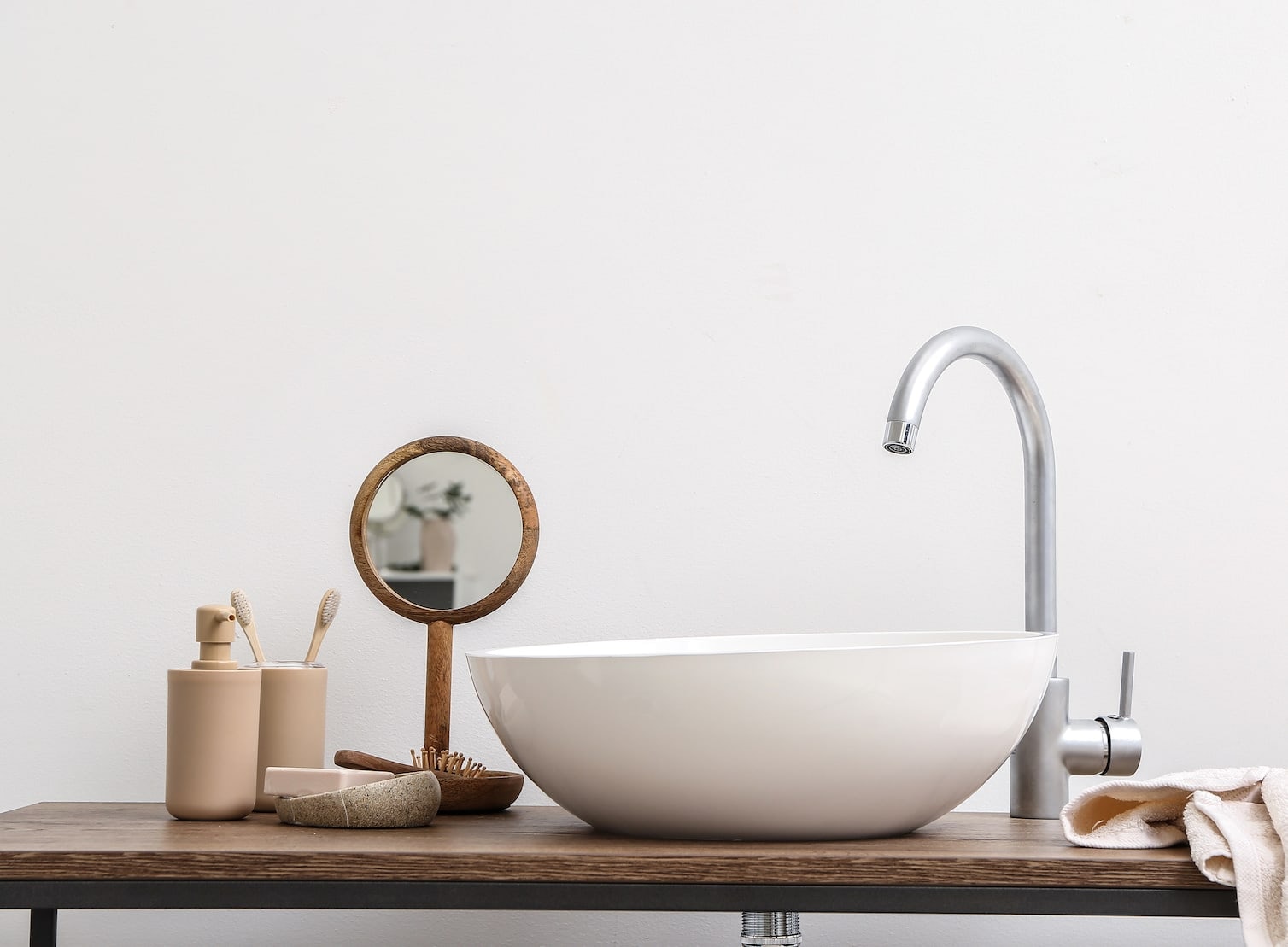 A countertop basin on a wooden shelf with a round mirror and small bathroom accessories.