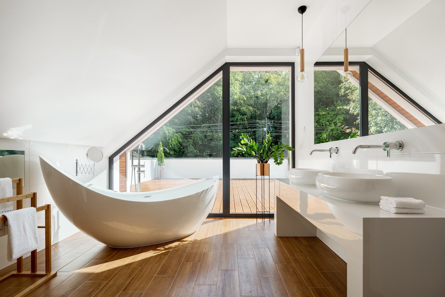 A loft bathroom with a freestanding slipper bath on a wooden floor beneath a glazed gable.