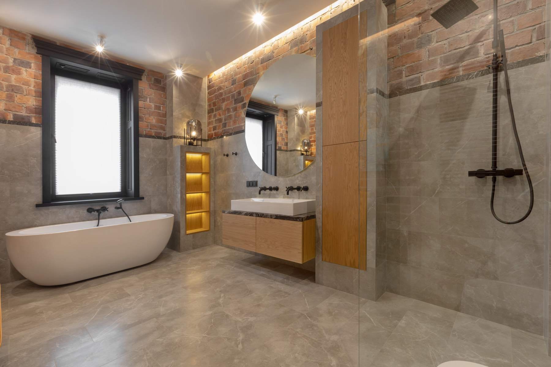 A wet room with a level-access shower and a freestanding bath, lit warmly beside exposed brick.