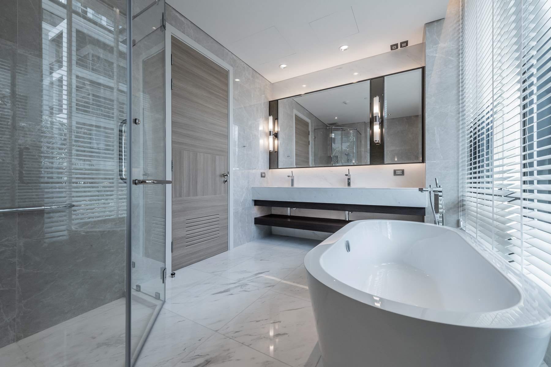A bright bathroom with a freestanding bath, a glass shower enclosure and a wide mirror over a double vanity.