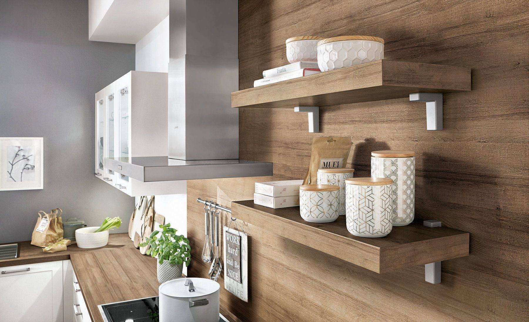 Detail of Nobilia open shelving in a modern kitchen, with wood-effect wall panelling and matching shelf boards on metal brackets, styled with ceramic canisters and cookbooks beside white units and a stainless steel extractor.