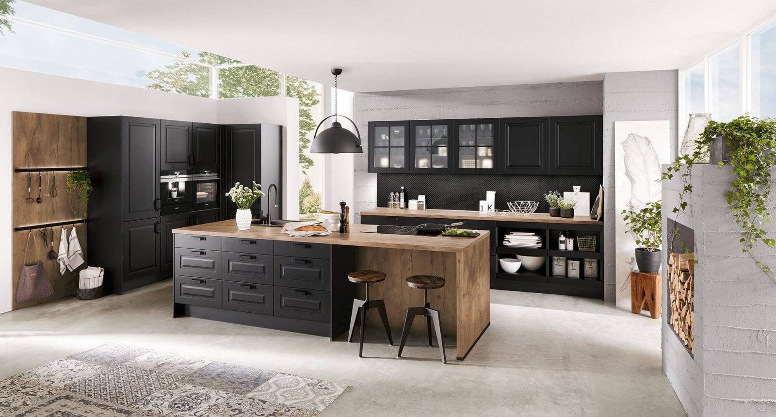 Nobilia open-plan kitchen with a matt black wood shaker design, featuring a large island with wood-effect panels, a black tap, and integrated ovens, plus open shelving and wall cabinets.